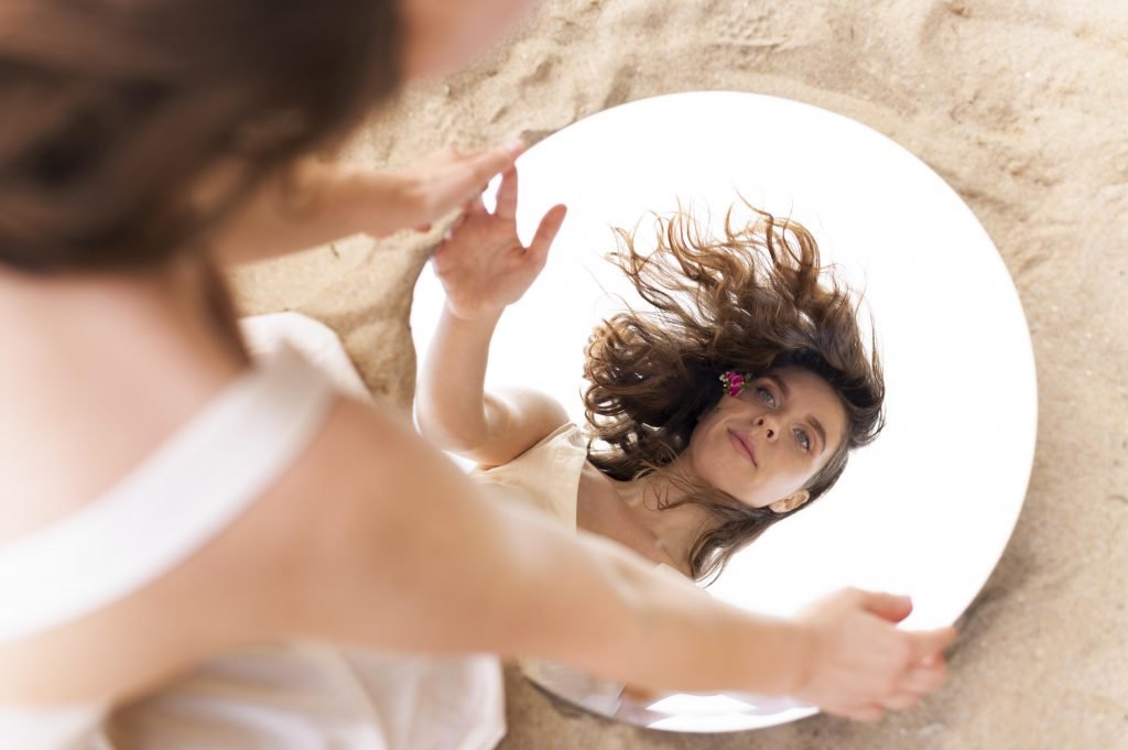 Mujer reflejada en un espejo sobre la arena, imagen conceptual sobre la identidad y el autoconocimiento – Ana Serrano Psicóloga.