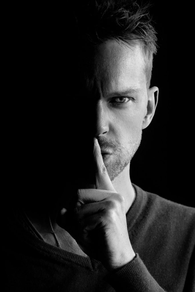 Retrato en blanco y negro de un hombre con gesto de silencio, representando el control emocional en personas narcisistas – Ana Serrano Psicóloga.